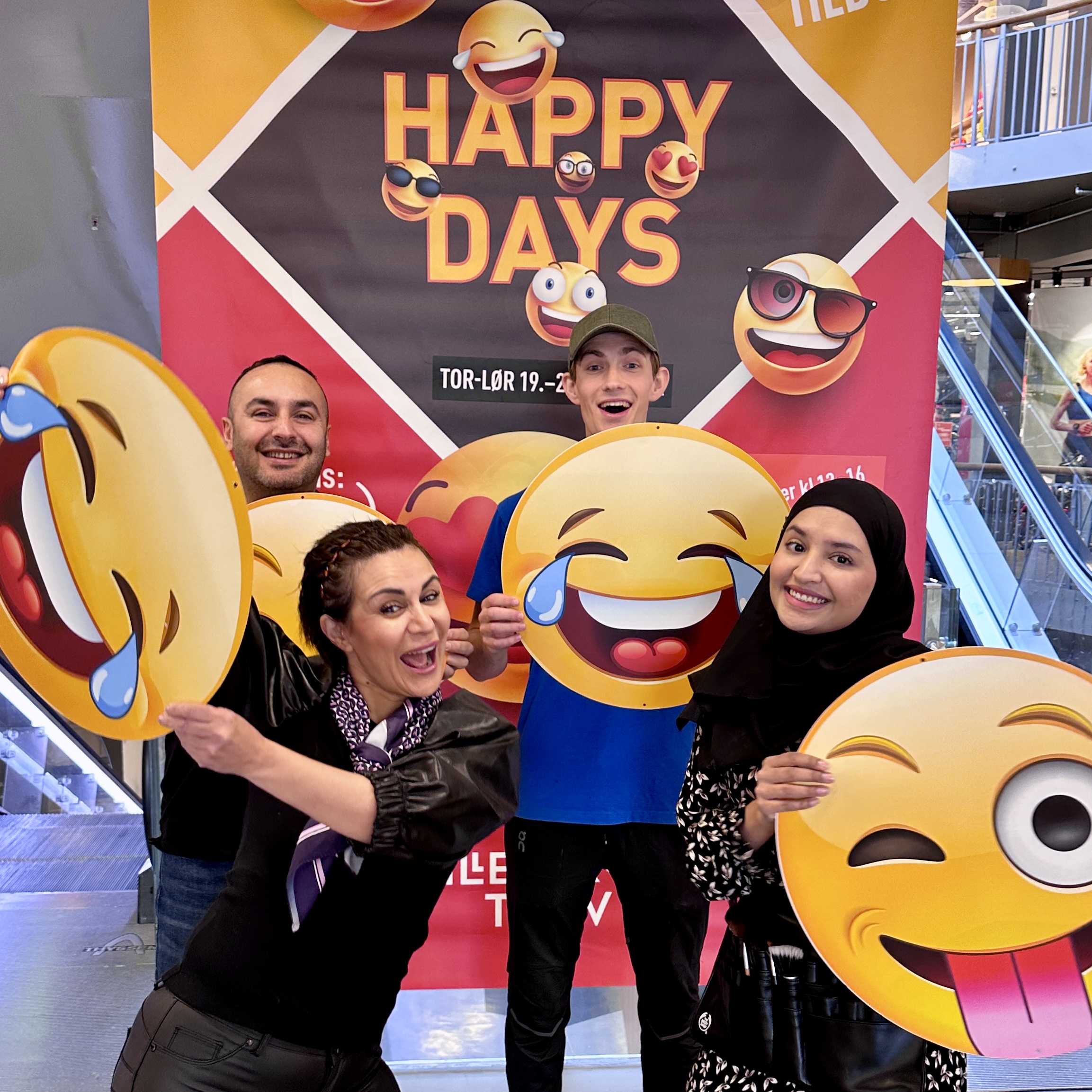 Happy Days med blide fjes og glade tilbud! 4 butikkansatte med hver sin smilefjesplakat foran stort Happy Days plakat
